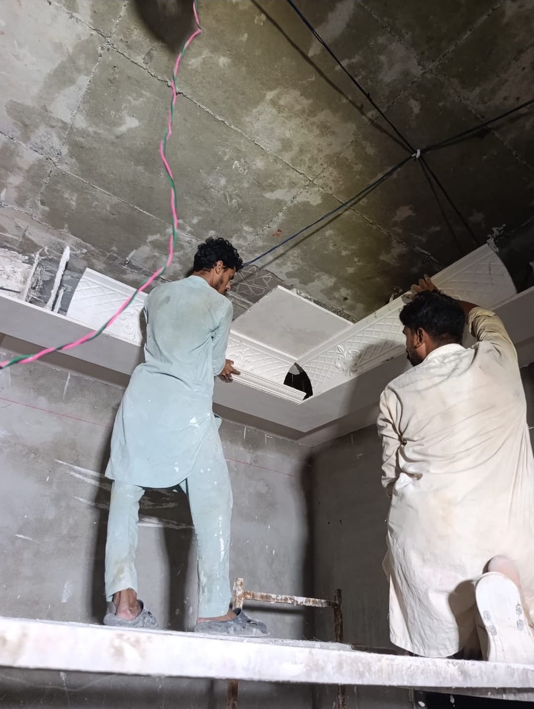 Two workers on a scaffold fixing ceiling boards under a bare concrete slab