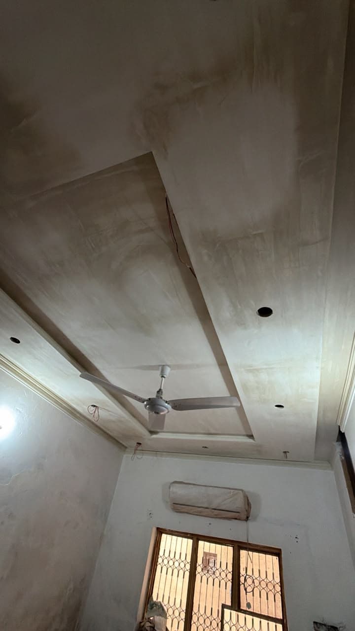 A stepped gypsum false ceiling over a room with a split AC and a fan