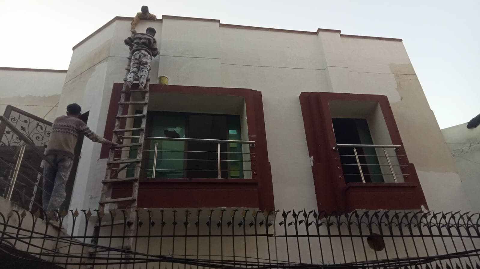 The same house front painted cream with maroon window surrounds, a painter finishing the top