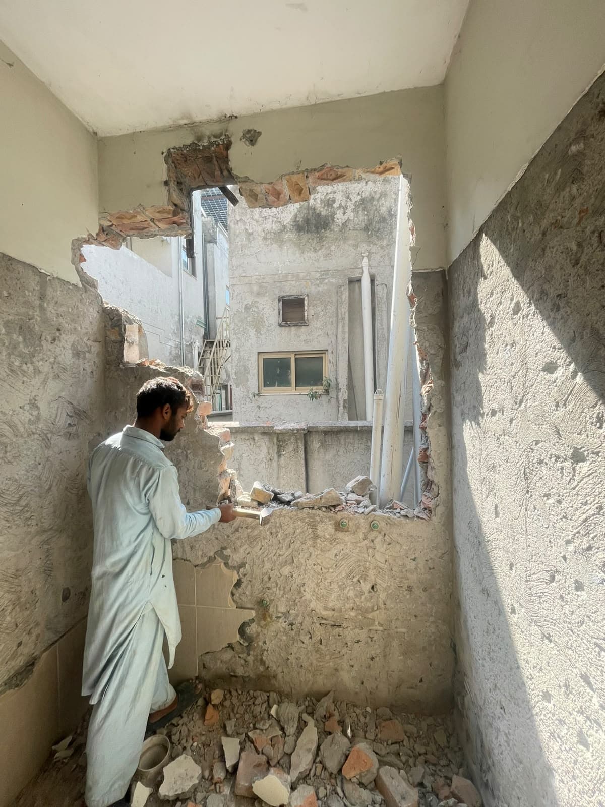 A worker cutting a new window opening through a wall at House #162