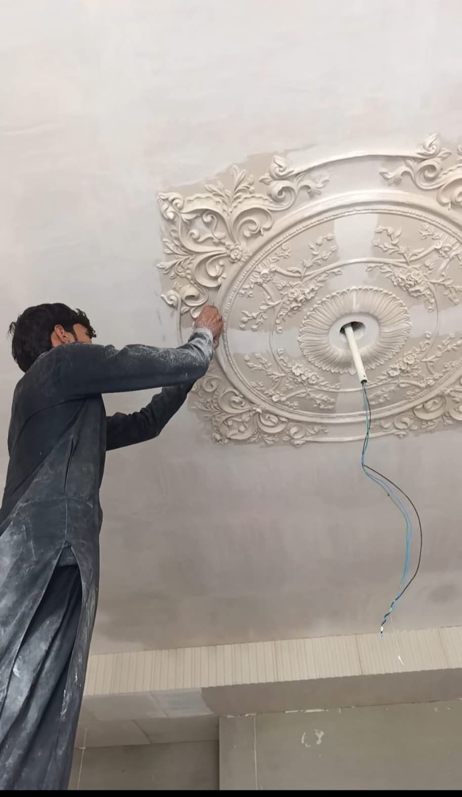 A worker fitting a large ornamental plaster medallion to a ceiling