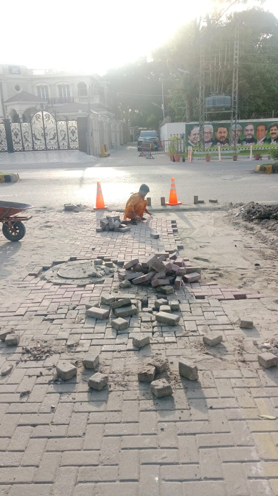 A worker relaying tuff tiles by hand at a roadside junction, with lifted tiles stacked nearby
